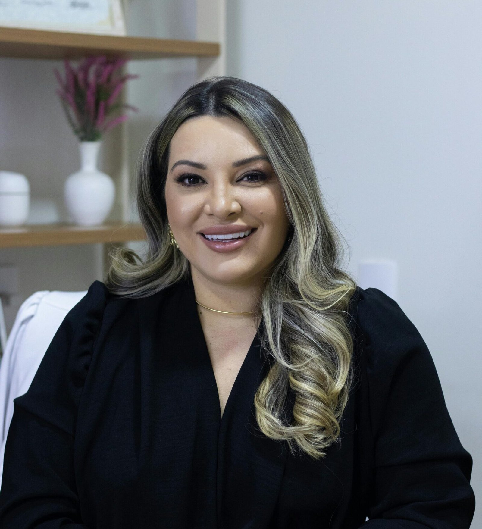 Confident woman in black attire smiling at desk with coffee cup, indoors.